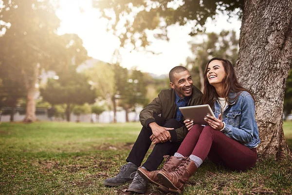 Mañanas pacíficas juntos. Foto de una alegre pareja joven sentada debajo de un árbol con una tableta digital afuera en un parque. —  Fotos de Stock