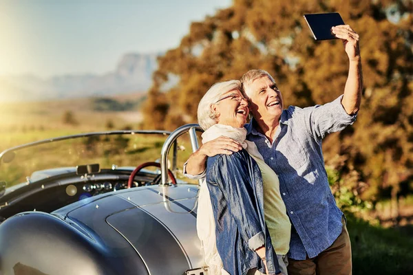 Tar en selfie till barnbarnen. Skjuten av ett äldre par poserar för en selfie medan ute på en roadtrip i en cabriolet. — Stockfoto