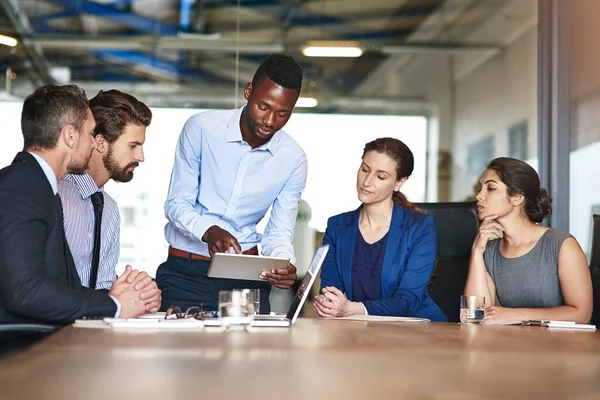 Es un hombre con ideas. Fotografía de un grupo de colegas corporativos hablando juntos sobre una tableta digital en una oficina. — Foto de Stock