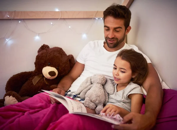 Ze kan niet slapen zonder dat papa haar een verhaal voorleest. Gehakt schot van een vader die een boek leest met zijn kleine dochter in bed thuis. — Stockfoto