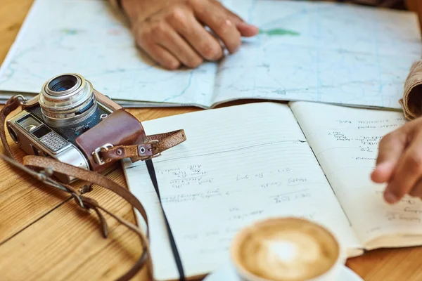 O diário de viagem mantém-no no caminho certo. Tiro de um turista não identificável olhando para mapas e diários de viagem enquanto desfruta de café em um café. — Fotografia de Stock