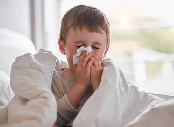 My nose wont stop dripping. Shot of a little boy feeling ill in bed at home and blowing his nose. — Stock Photo, Image