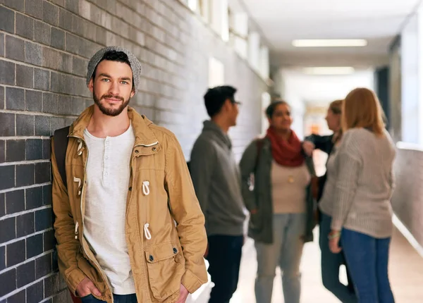 Leuke vent op de campus. Portret van een jonge mannelijke universiteitsstudent in een campusgang met zijn klasgenoten op de achtergrond. — Stockfoto