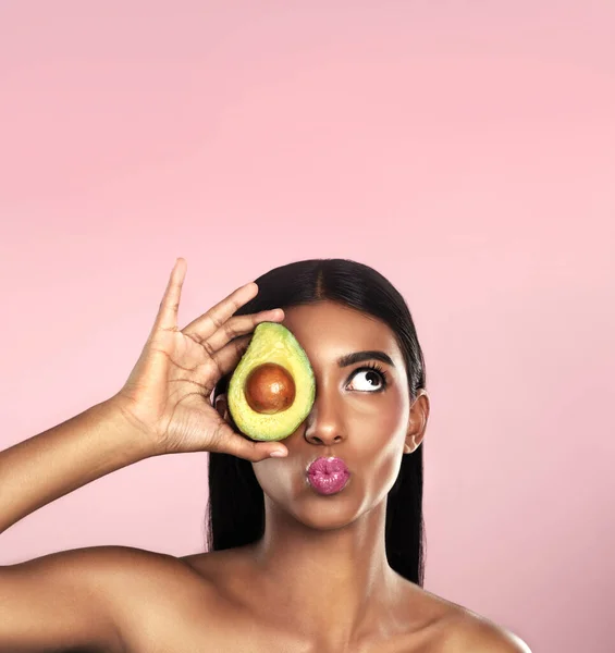 Haar huid verbeteren, één avocado tegelijk. Studio shot van een mooie jonge vrouw poseren met een avocado tegen een roze achtergrond. — Stockfoto