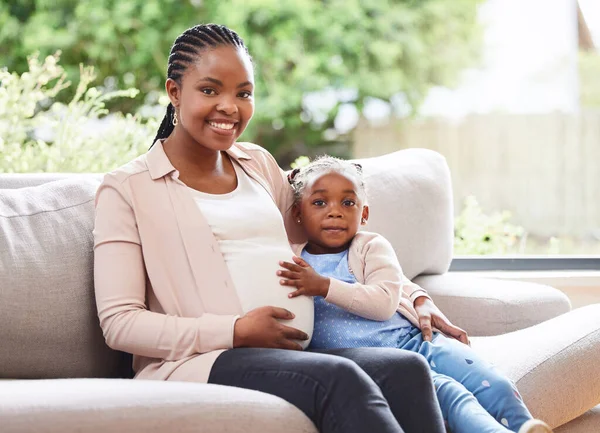 Jag tyckte det var dags för en till. Beskärda porträtt av en attraktiv ung gravid kvinna och hennes dotter sitter i soffan hemma. — Stockfoto