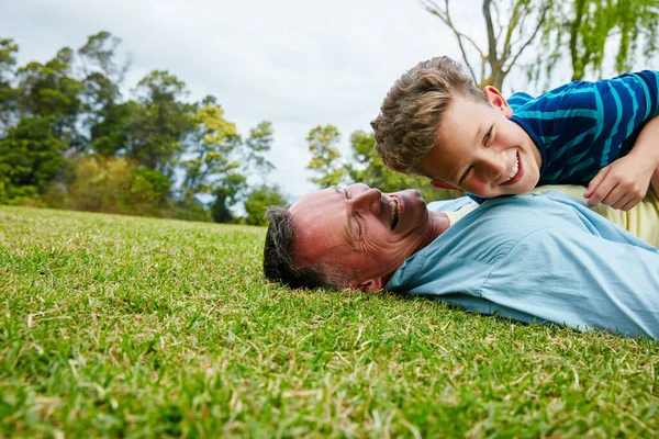 Μοιραζόμαστε στιγμές μεταξύ πατέρα και γιου. Πυροβολισμός ενός γελαστού πατέρα και γιου ξαπλωμένου στο γρασίδι.. — Φωτογραφία Αρχείου