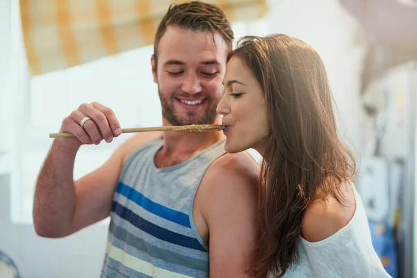 Är det kärlek jag smakar. Skjuten av en glad ung man erbjuder sin flickvän en smak av hans matlagning hemma. — Stockfoto