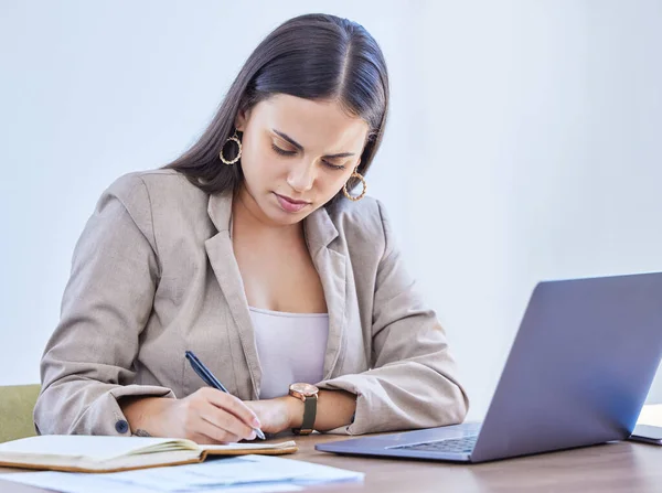 Mise à jour de son journal avec quelques notes importantes. Prise de vue d'une jeune femme d'affaires écrivant des notes tout en travaillant sur un ordinateur portable dans un bureau. — Photo