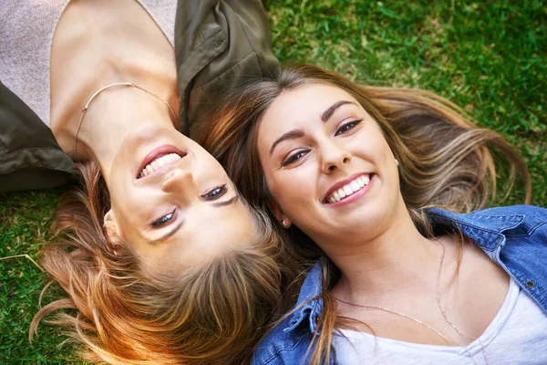 Vänner är vad som verkligen gör sommaren. Hög vinkel porträtt av två attraktiva unga kvinnor som ligger på gräset utanför. — Stockfoto