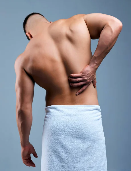 내 연골 이 있는 곳이야. 신원을 알 수없는 남자가 회색 배경에 샤워를 한 후 허리 통증을 겪고 있는 리어 뷰 사진. — 스톡 사진