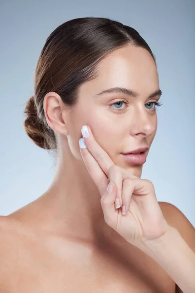 Haltet ihre Haut schön und gesund. Studioaufnahme einer attraktiven jungen Frau, die ihr Gesicht vor grauem Hintergrund befeuchtet. — Stockfoto