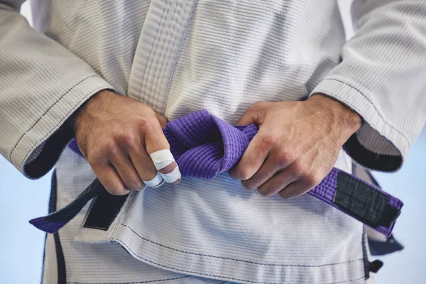 C'est un professionnel chevronné. Plan recadré d'un homme méconnaissable attachant une ceinture violette autour de sa taille alors qu'il était en plein jiu jitsu gi. — Photo