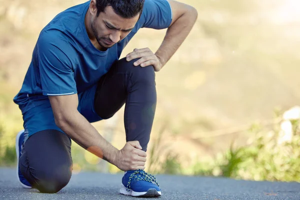 Mi servono scarpe da corsa migliori. Colpo di un bel ragazzo inginocchiato e affetto da una caviglia slogata durante il suo allenamento all'aperto. — Foto Stock