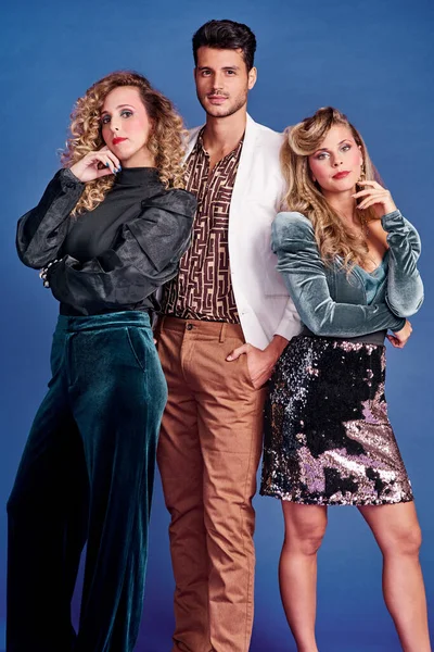 Lähdemme 80-luvun teemajuhliin. Kolme nuorta poseeraa yhdessä 80-luvun vaatteissa sinistä taustaa vasten. — kuvapankkivalokuva