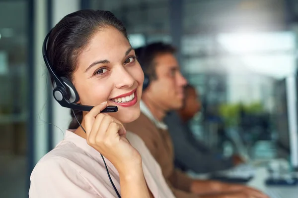 Uitstekende klantenservice gaat een lange weg. Portret van een call center agent die in een kantoor werkt met haar collega 's op de achtergrond. — Stockfoto