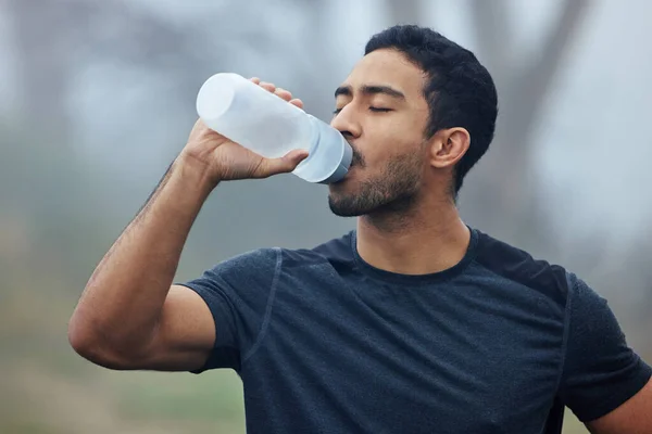 Taking a break to replenish his energy. Shot of a sporty young man drinking water while exercising outdoors.