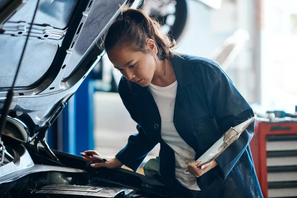 Shell le da la mejor y menos costosa solución para los problemas de su coche. Fotografía de una mujer mecánica trabajando en un coche en un taller de reparación de automóviles. —  Fotos de Stock