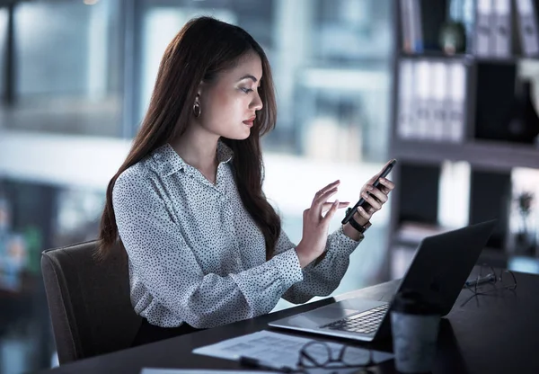 Parfois, le succès demande un peu plus de temps. Prise de vue d'une jeune femme d'affaires utilisant un téléphone portable pendant qu'elle travaillait dans un bureau la nuit. — Photo