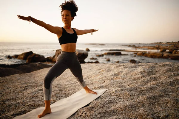 你可以通过瑜伽达到你的目标。一名年轻貌美的女子日落时分在海滩练瑜伽的全景照片. — 图库照片