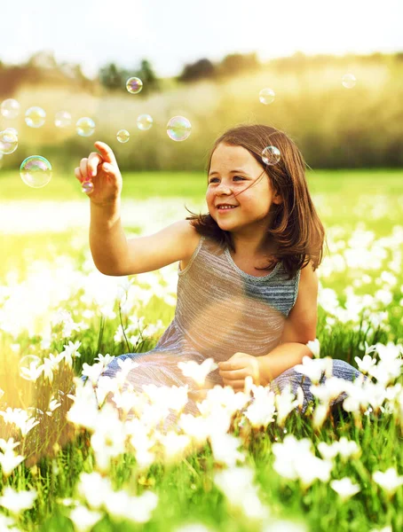 Güneşin altında biraz eğleniyoruz. Dışarıda kır çiçekleriyle dolu bir tarlada baloncuklarla oynayan sevimli küçük bir kızın fotoğrafı.. — Stok fotoğraf