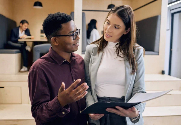 He values her opinion. Cropped shot of two young businesspeople looking over paperwork with their colleagues in the background. — Stock Photo, Image
