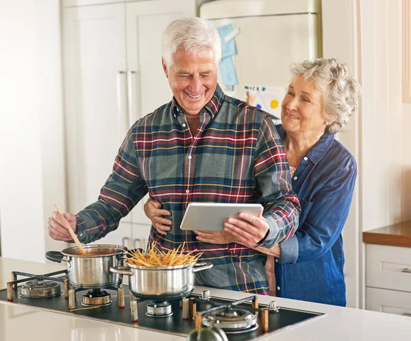 Чому готують, добре виглядають. Обрізаний знімок старшої пари, використовуючи цифровий планшет, готуючи разом на своїй кухні вдома . — стокове фото
