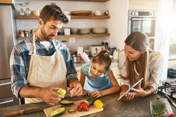 Együtt elsajátítani egy új technikát. Két boldog szülő és a kislányuk együtt próbálnak ki egy új receptet a konyhában.. — Stock Fotó