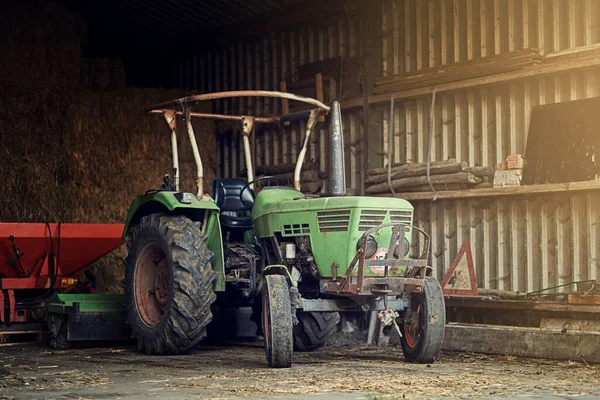 Ninguna granja está completa sin una. Un disparo de un viejo tractor oxidado parado en un granero vacío. — Foto de Stock