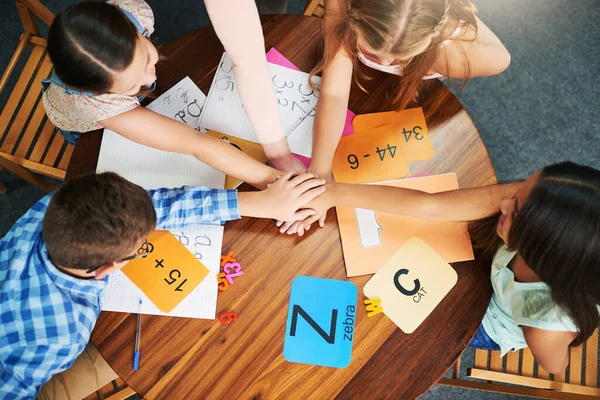 Hagamos este equipo. Foto de ángulo alto de un grupo de escolares alegres que forman un grupo con las manos dentro del aula durante el día. —  Fotos de Stock