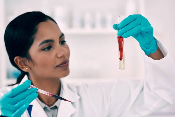 Посмотрим, как эта кровь отреагирует с этой жидкостью. Обрезанный снимок привлекательной молодой женщины-ученого, осматривающей образец крови в пробирке во время работы в лаборатории. — стоковое фото