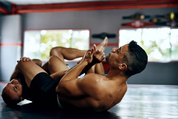 You must know your opponents weakness and abuse it. Shot of two male fighters wrestling on the floor at the gym. — Stock Photo, Image