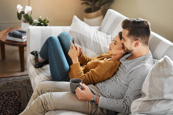 Lets see what shows are trending on social media. Shot of a young couple using a cellphone while relaxing on the sofa at home. — Stock Photo, Image
