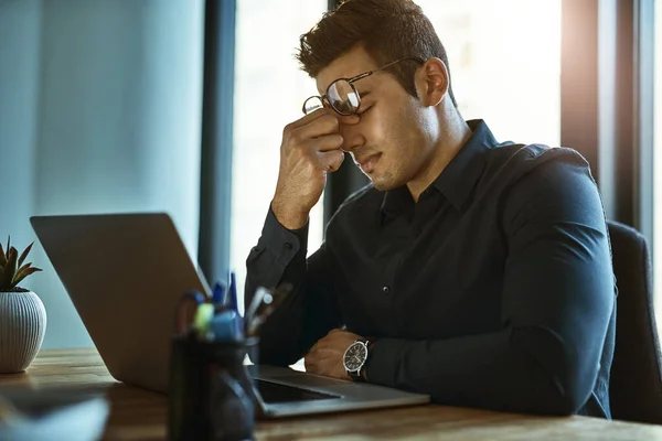Kiedy stres w pracy wywołuje silne migreny. Strzał młodego biznesmena wyglądającego na zestresowanego podczas pracy na laptopie w biurze. — Zdjęcie stockowe
