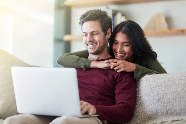 En lo que estás trabajando. Foto de una pareja joven y cariñosa usando su computadora portátil mientras se relaja en el sofá en casa. —  Fotos de Stock