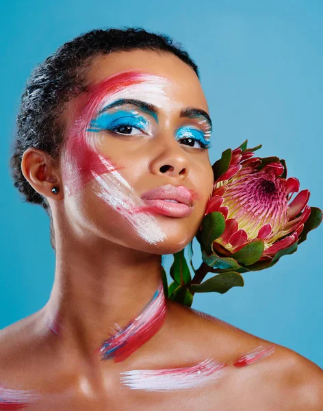 Kolorowe. Zupełnie jak kwiat. Studio portret pięknej młodej kobiety pokrytej farbą do twarzy na niebieskim tle. — Zdjęcie stockowe