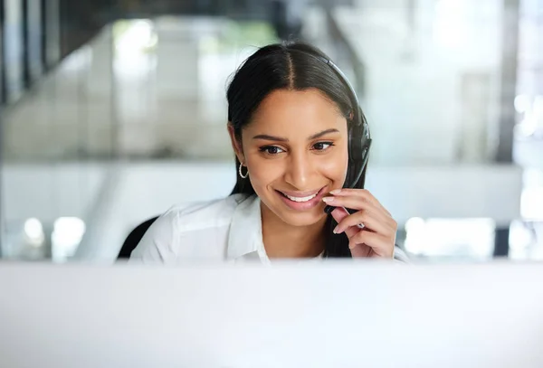 Jag är glad att jag kunde hjälpa till. Skjuten av en attraktiv ung call center agent sitter på kontoret och bär ett headset när du använder hennes dator. — Stockfoto