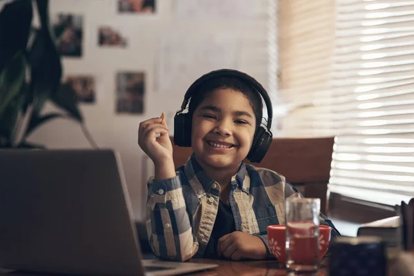 El descanso es la hora de la merienda. Foto de un niño adorable usando una computadora portátil y auriculares mientras completaba una tarea escolar en casa. — Foto de Stock