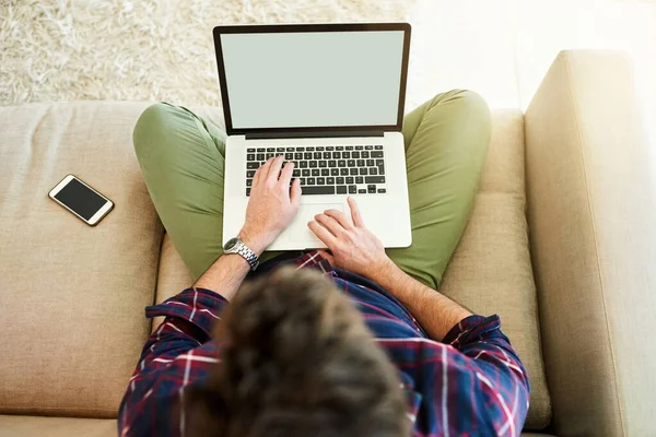 Ponte cómodo, conéctate. Foto de ángulo alto de un hombre joven usando una computadora portátil en el sofá en casa. — Foto de Stock