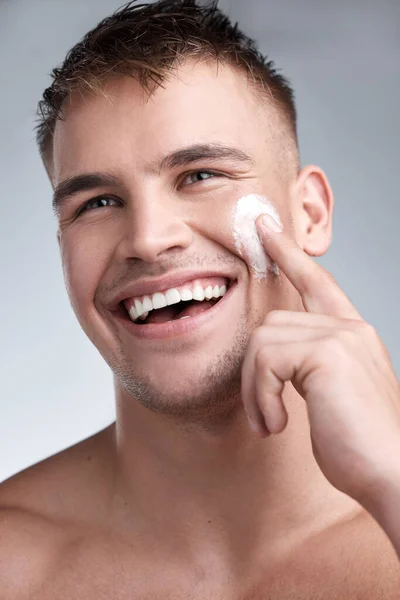 Take your skin back to yesterday, every day. Cropped closeup shot of an attractive young man applying moisturiser to his face against a grey background. — Stock Photo, Image