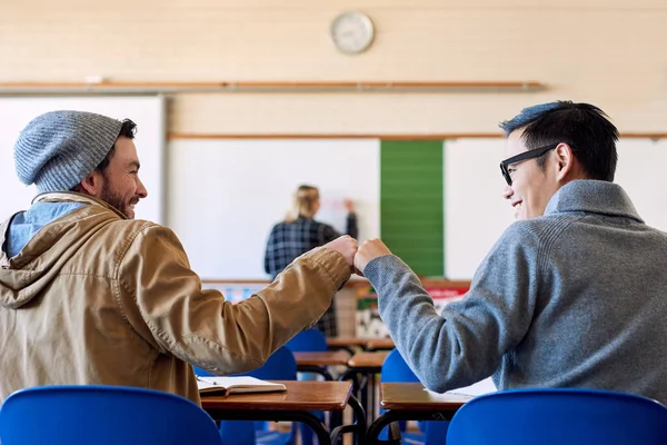 Ja, broer. Achteraanzicht opname van twee jonge mannelijke studenten vuist stoten in de klas tijdens een lezing. — Stockfoto