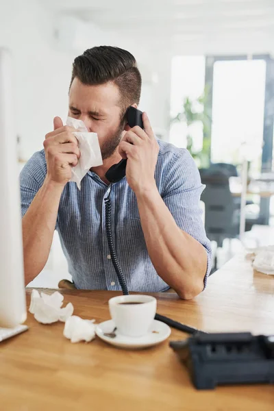 O frio deixou-o muito congestionado. Tiro cortado de um jovem empresário soprando o nariz enquanto falava ao telefone em um escritório. — Fotografia de Stock