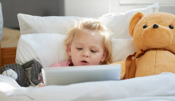 Ismerek egy gyerekdalocskát, amit játszhatok. Egy imádnivaló kislányról, aki az ágyban fekszik egy digitális tablettel.. — Stock Fotó