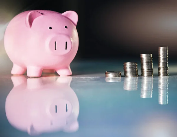 Un poco de ahorro va muy lejos. Tiro de una hucha y monedas apiladas en un escritorio en una oficina vacía. — Foto de Stock