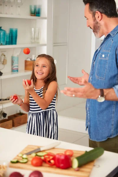 Jantar e um espetáculo Agora isso é estrondo para o seu dinheiro. Tiro de uma menina adorável malabarismo tomates enquanto cozinha com seu pai em casa. — Fotografia de Stock