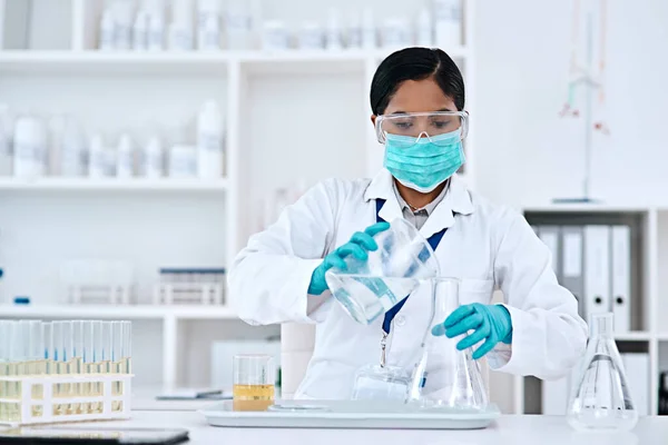 解決策はあなたの手にあります。研究室で働いている間にビーカーから円錐形のフラスコに透明な液体を転送する魅力的な若い女性科学者の作物のショット. — ストック写真