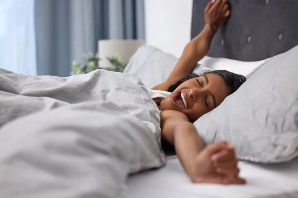 Von guter Laune keine gute Nachtruhe. Aufnahme einer jungen Frau, die in ihrem Bett gähnt und sich dehnt. — Stockfoto