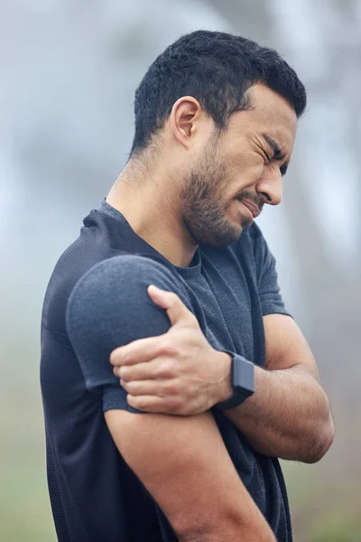 This pain is becoming more unbearable by the minute. Shot of a sporty young man holding his shoulder in pain while exercising outdoors. — Stock Photo, Image