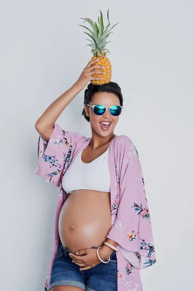 Eine Mutter mit feinem Apfel zu sein. Studioaufnahme einer schönen jungen Schwangeren mit einer Ananas auf dem Kopf vor grauem Hintergrund. — Stockfoto