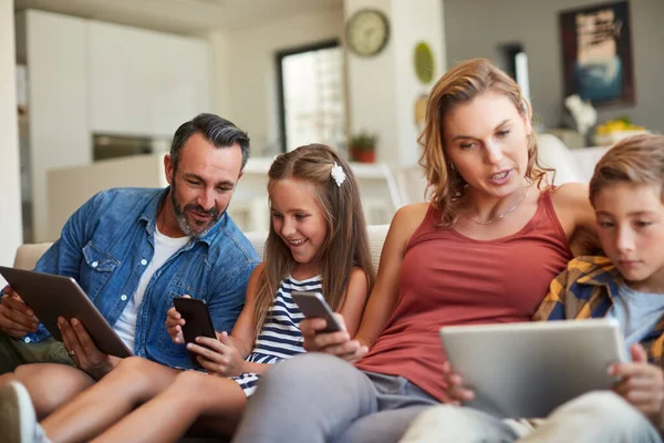A családi idő jövője most van. Egy boldog fiatal családról készült felvétel, aki vezeték nélküli eszközöket használ otthon a kanapén. — Stock Fotó