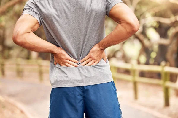 Look back on your setbacks and find the lessons in them. Shot of an unrecognisable man experiencing back pain while working out in nature. — Stock Photo, Image